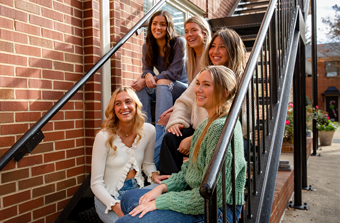Collegiate women together on a set of stairs outside together